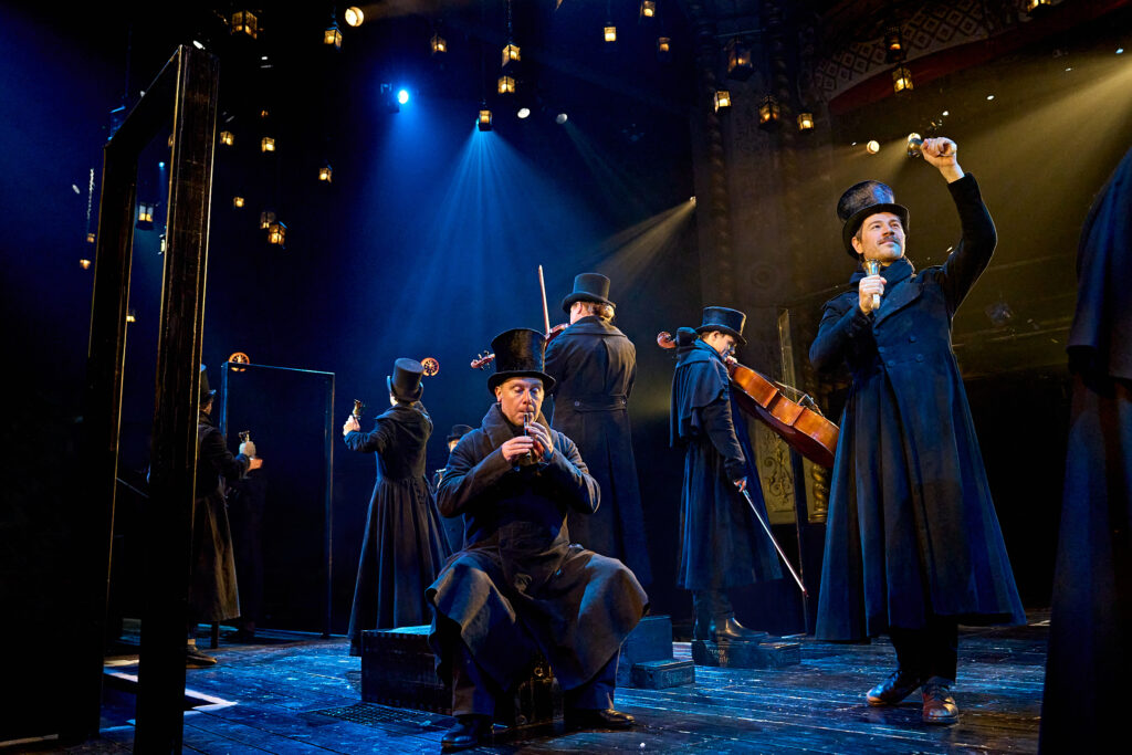 The ensemble of A Christmas Carol perform with hand bells, a whistle and a cello