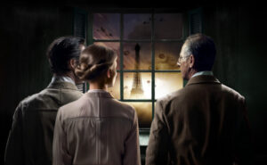 Two men and one woman look ahead with the Eifflel tower visible through the window in front of them